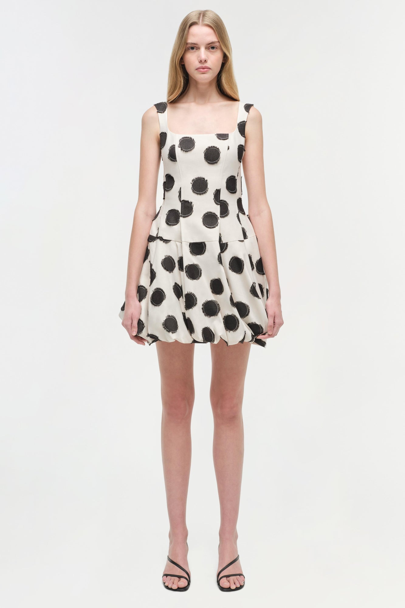White sleeveless mini dress with black polka dot pattern and gathered skirt hem.