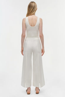 Woman wearing cream-colored cropped cotton pants with a scoop-neck tank top, shown from behind.