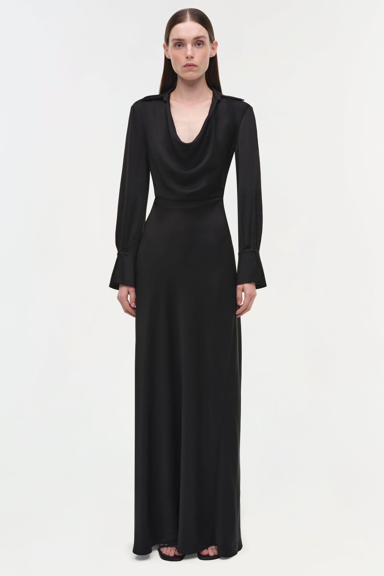 Black satin gown with draped cowl neckline, long sleeves with flared cuffs, and floor-length skirt.