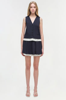 Woman wearing navy sleeveless button-front vest with pleated skort featuring white trim and matching white trim at waist.