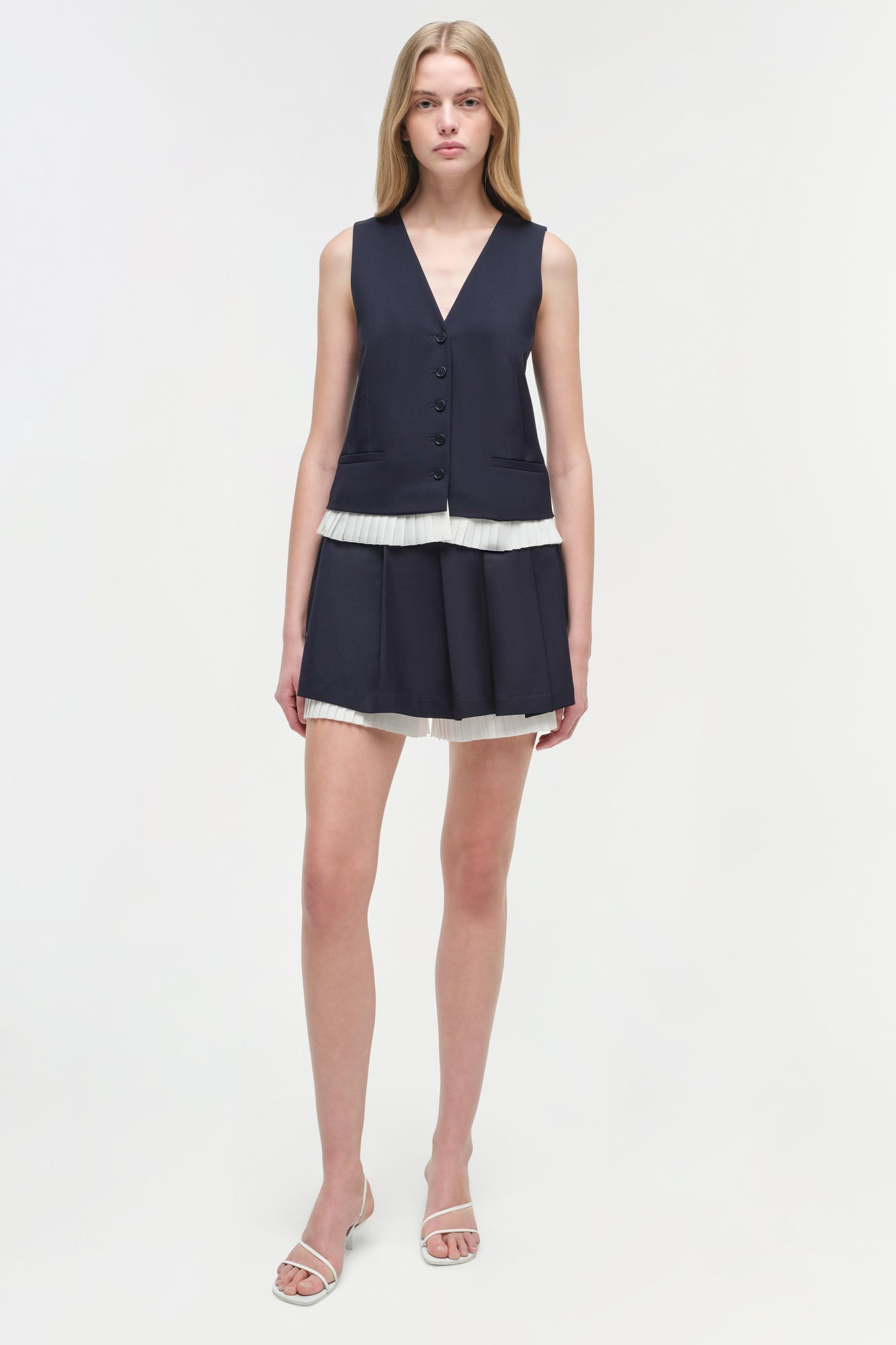 Woman wearing a navy pleated skort with white trim and matching buttoned vest over a white striped band.