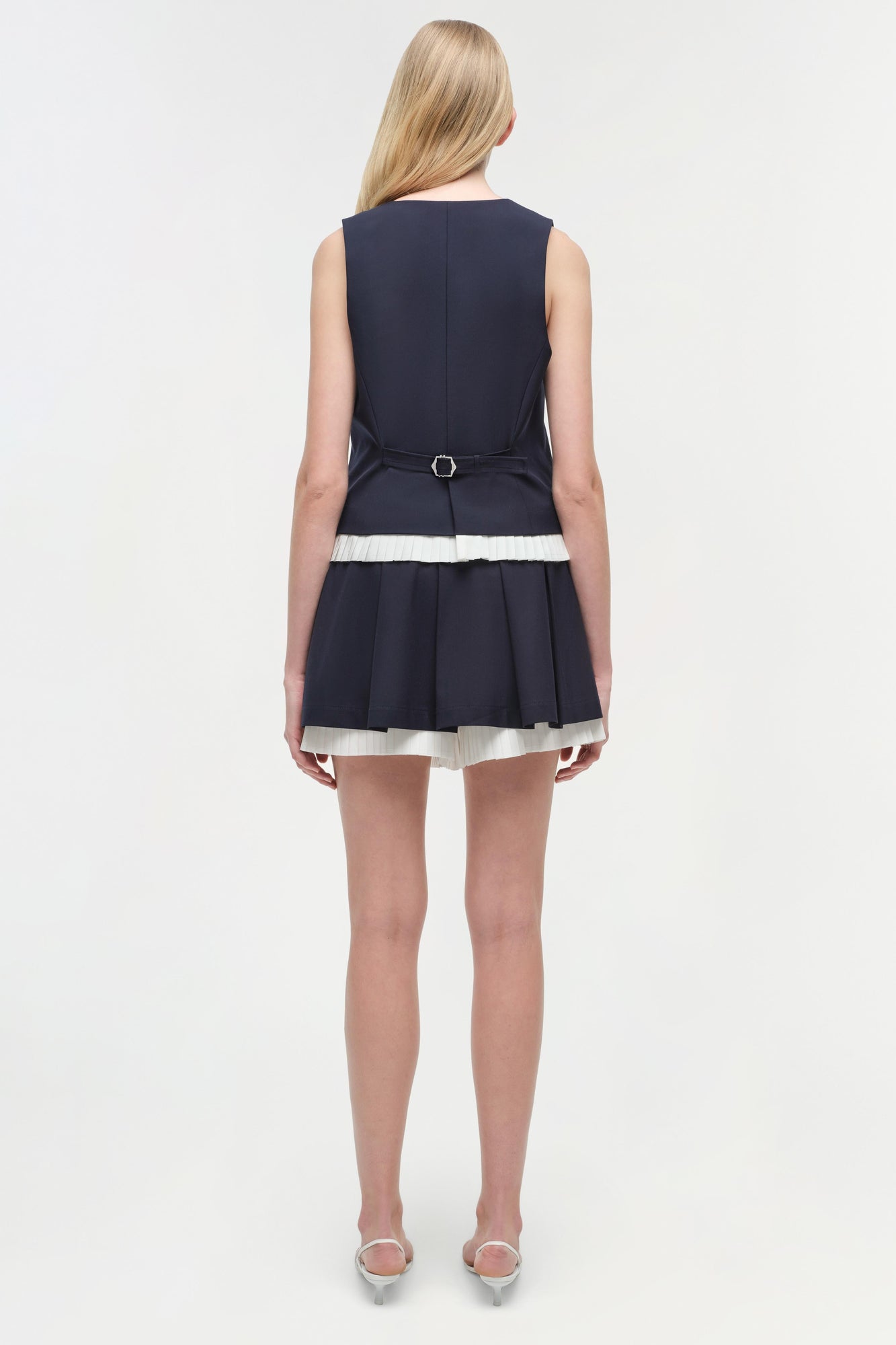 Navy pleated skort with white stripe trim, belted waist, sleeveless design, worn with clear heels.