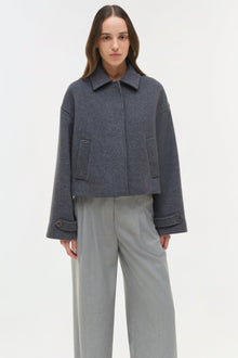 Woman wearing a charcoal wool jacket with a collar and button front, paired with light gray trousers.