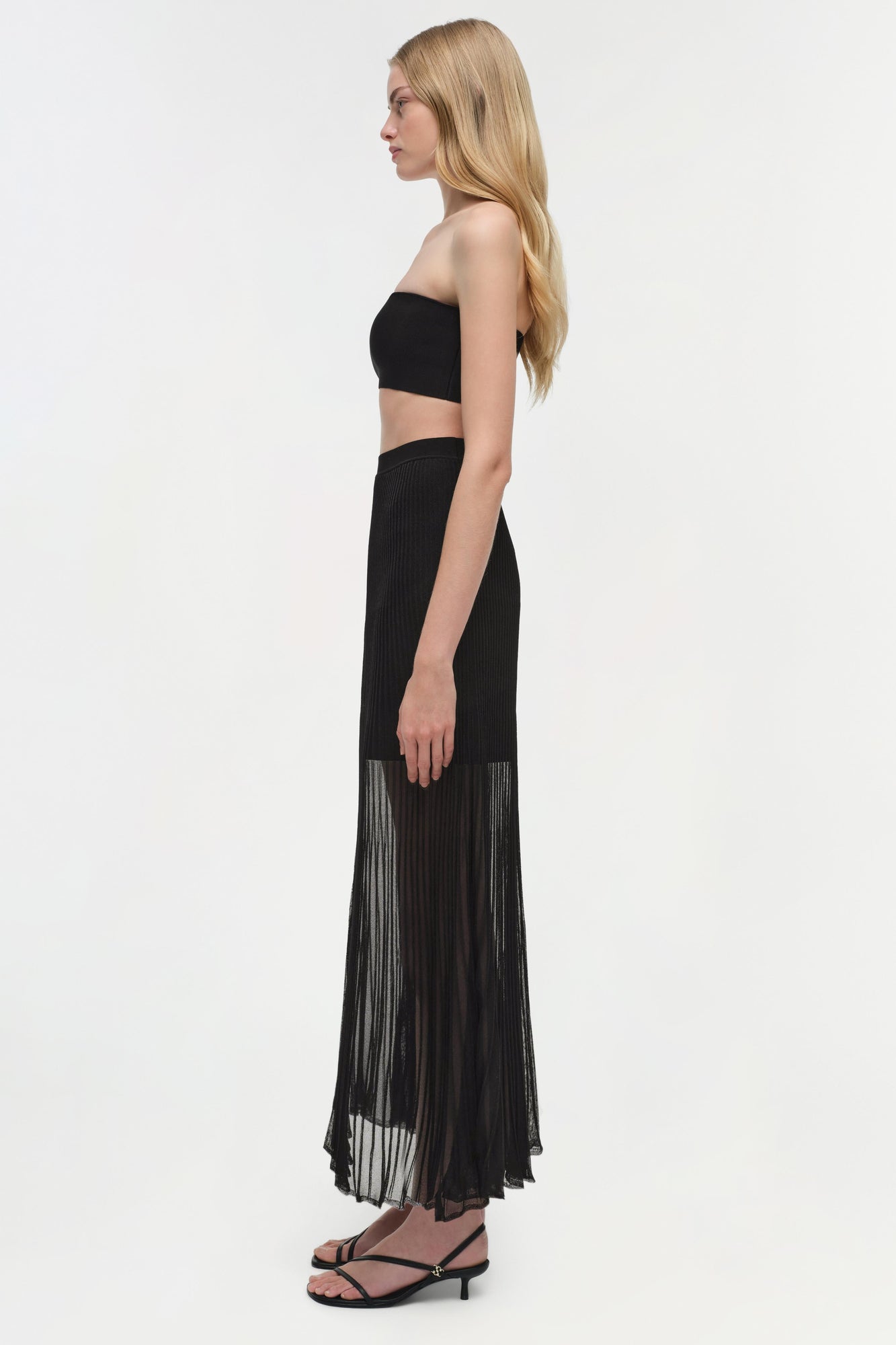 Black knit bralette with bandeau style and thin straps, worn with pleated skirt.
