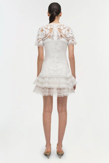 White lace dress with short sleeves, tiered ruffle skirt, and intricate lace detailing throughout, shown from back view.