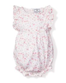 The Babys Twill Ruffled Romper in Dorset Floral by Petite Plume is a charming Victorian-inspired piece featuring pink flowers on white with ruffled sleeves, a gathered waist, and visible bottom buttons for classic elegance and modern comfort.