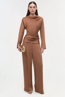 Woman wearing a tan satin top with draped ruching at the waist and long sleeves, paired with matching wide-leg pants.