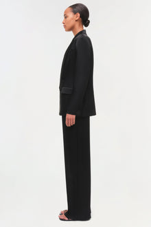 Black satin blazer with notch lapels and matching wide-leg pants worn by model in profile view.