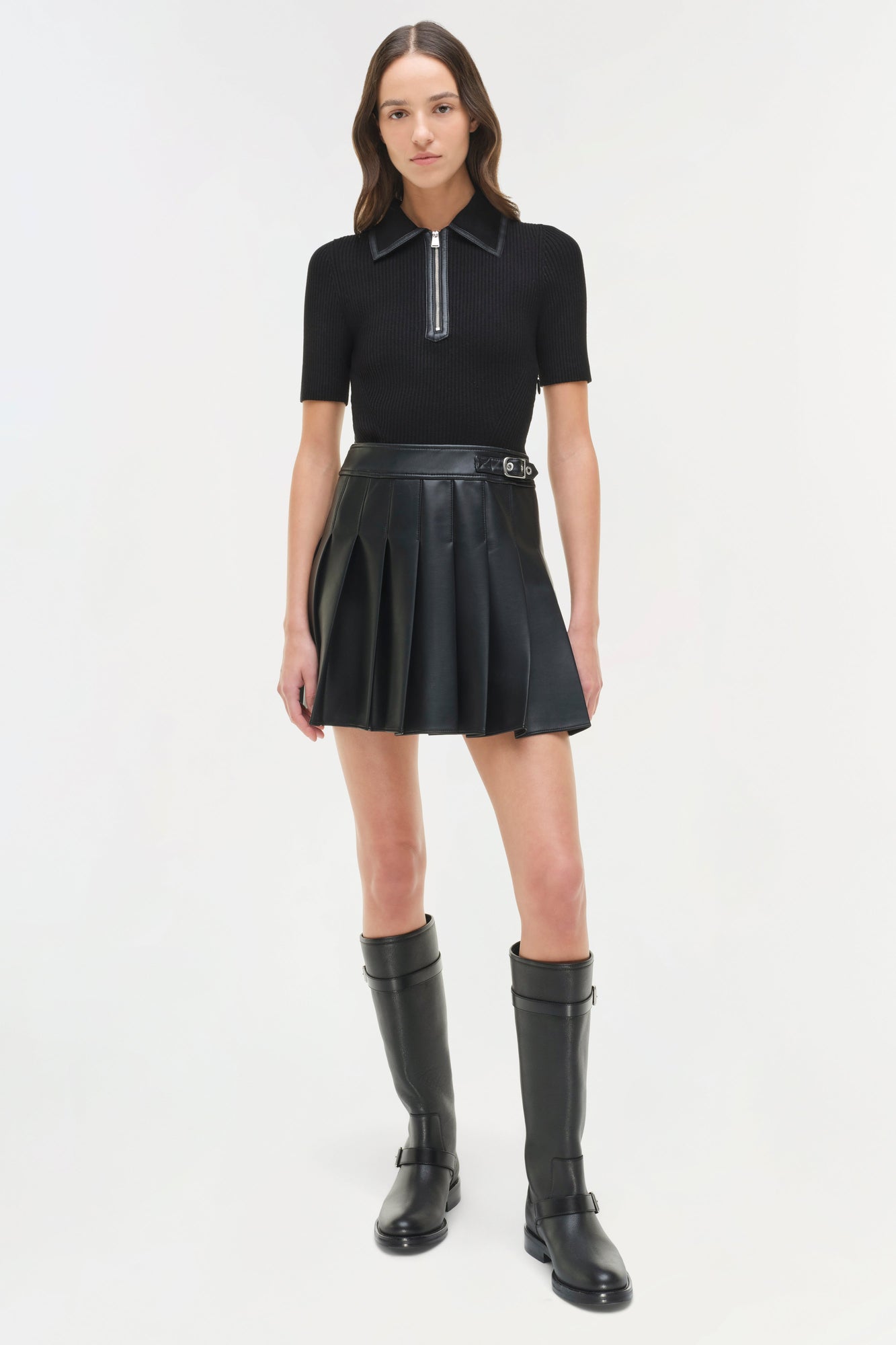 Black knit mini dress with collared polo top, half-zip closure, pleated leather skirt, and buckle belt detail.