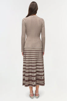Woman wearing a brown and cream ribbed knit cardigan with a geometric patterned pleated midi skirt, shown from behind.