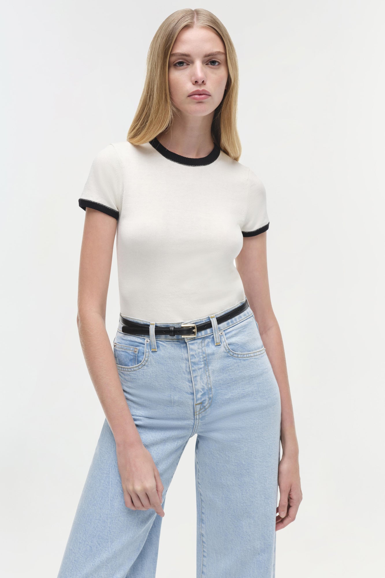 Cream short-sleeve top with black ribbed neckline and cuffs, worn with light-wash jeans.