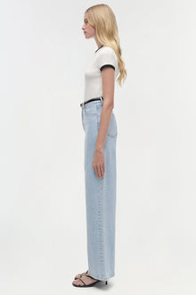 Woman wearing white short-sleeve top with navy trim and light blue straight-leg jeans, shown from the side.