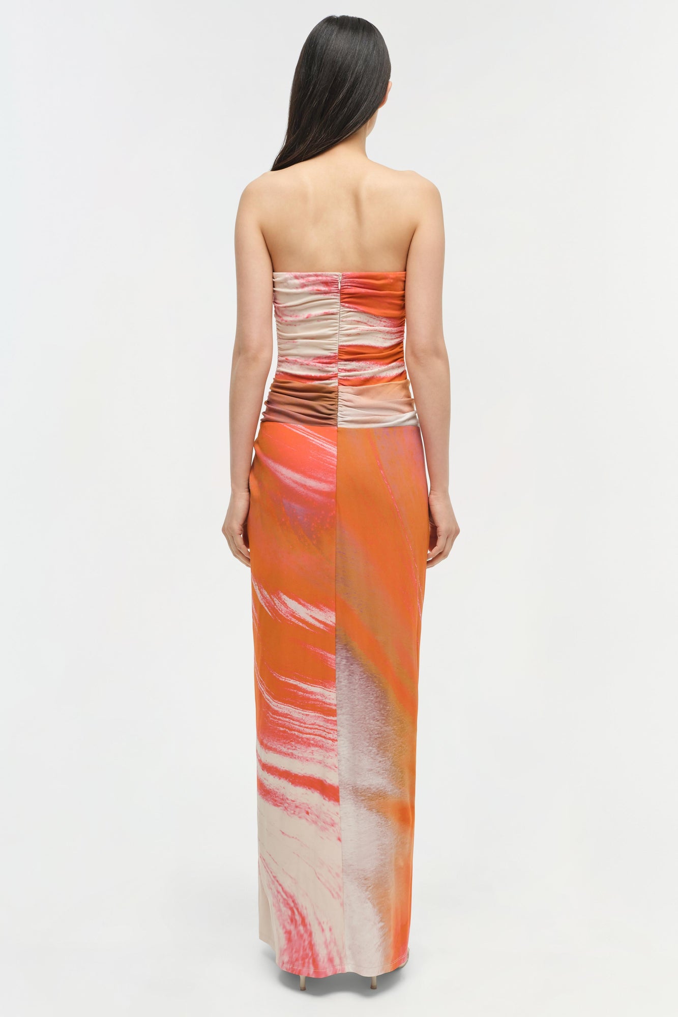 Strapless maxi gown with ruched bodice and orange, pink, and cream gradient print throughout.
