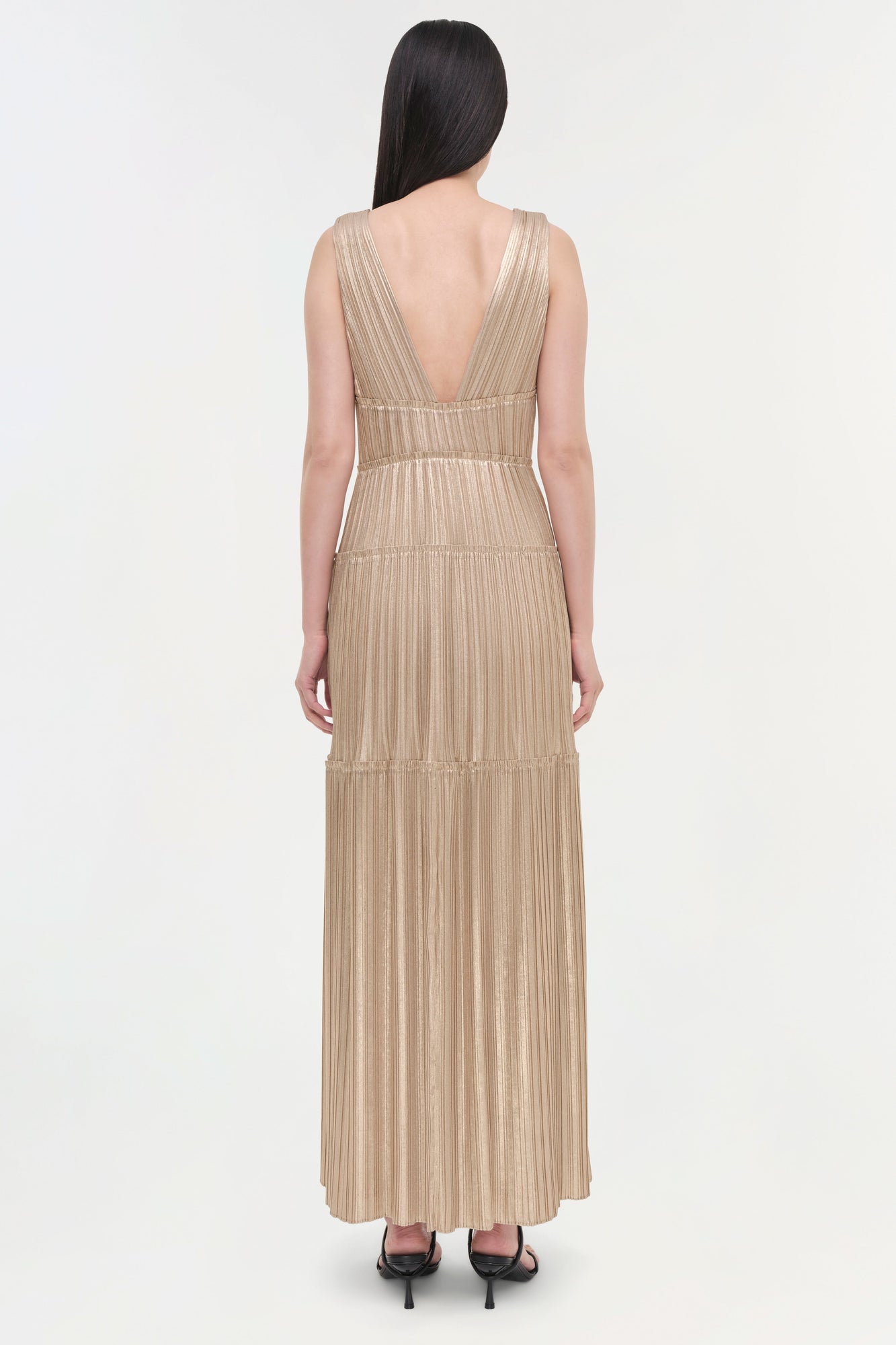 Beige sleeveless pleated gown with deep V-back and tiered skirt, shown from back view.