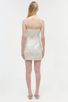 Ivory sequined mini dress with thin straps and open back, worn with metallic heels.