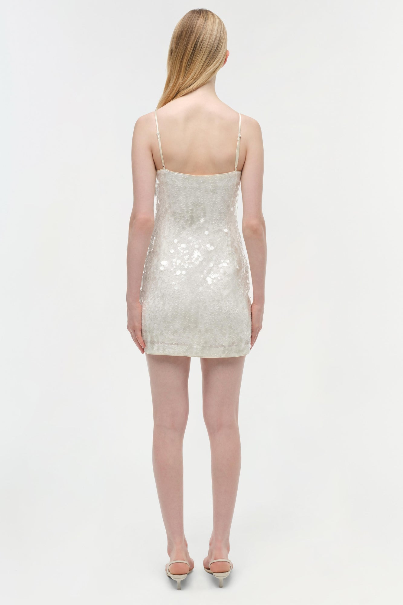 Ivory sequined mini dress with thin straps and open back, worn with metallic heels.