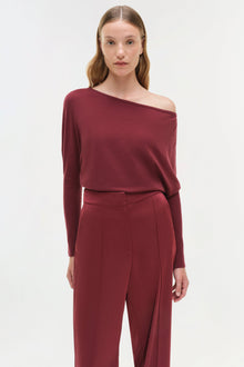 Burgundy off-shoulder sweater with long sleeves worn with matching high-waisted trousers.