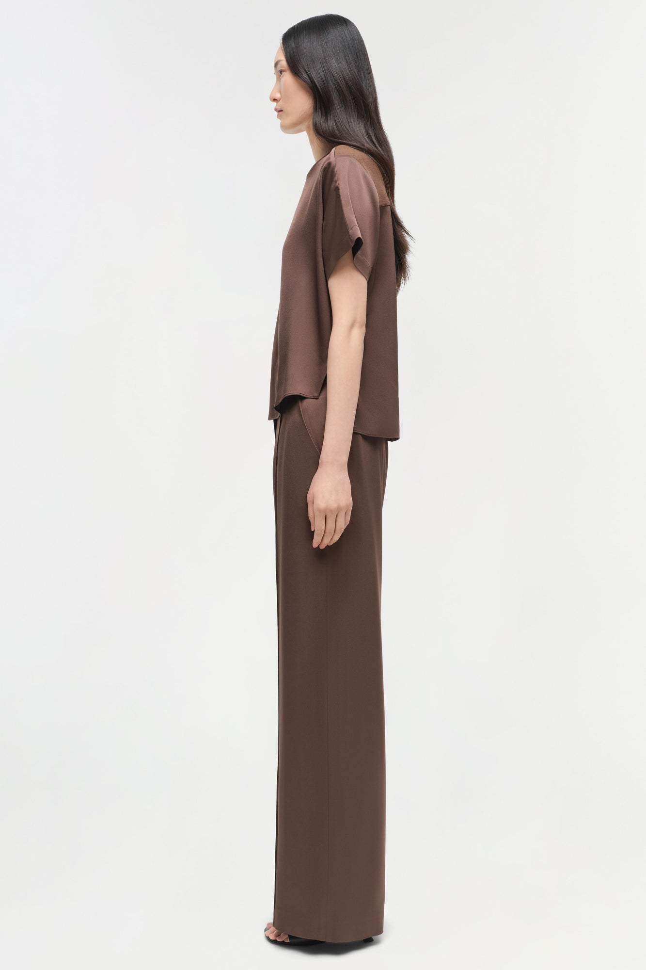 Brown satin t-shirt with short sleeves and draped front panel worn by model shown from side profile.