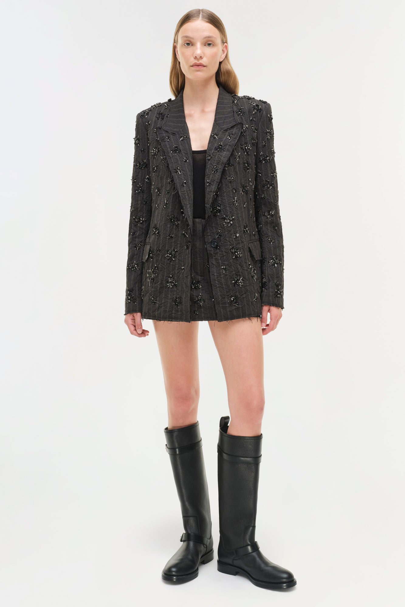 Charcoal blazer with all-over beaded embellishment, worn open over a black top, paired with black knee-high boots.