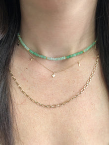 Closeup of woman's neck wearing a beaded chrysoprase necklace as a choker, a gold charm necklace with a hamsa, lightning bolt, star, moon, and evil eye, and a thick gold link chain