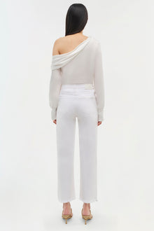Off-shoulder cream top with draped neckline and long sleeves, shown with white jeans.