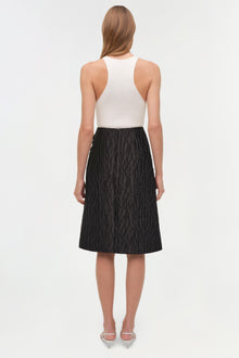 Woman wearing white sleeveless ribbed tank top and black textured jacquard midi skirt, back view.