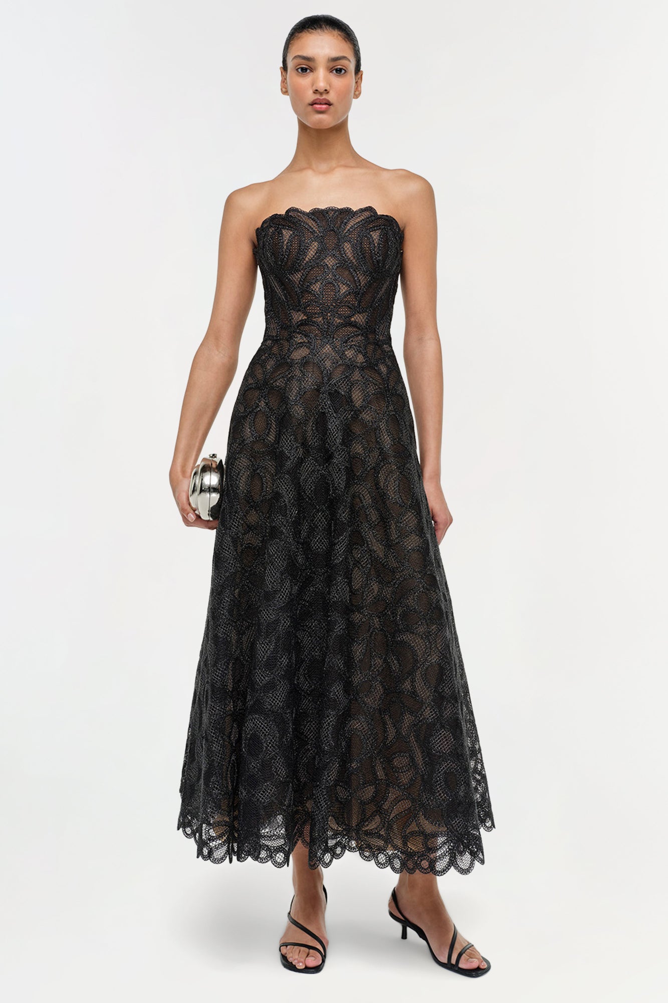 Black lace strapless midi dress with gilded pattern and scalloped hem on model wearing black heels.
