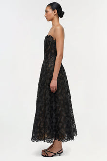 Black strapless lace midi dress with geometric pattern and scalloped hem, shown on model from side profile.