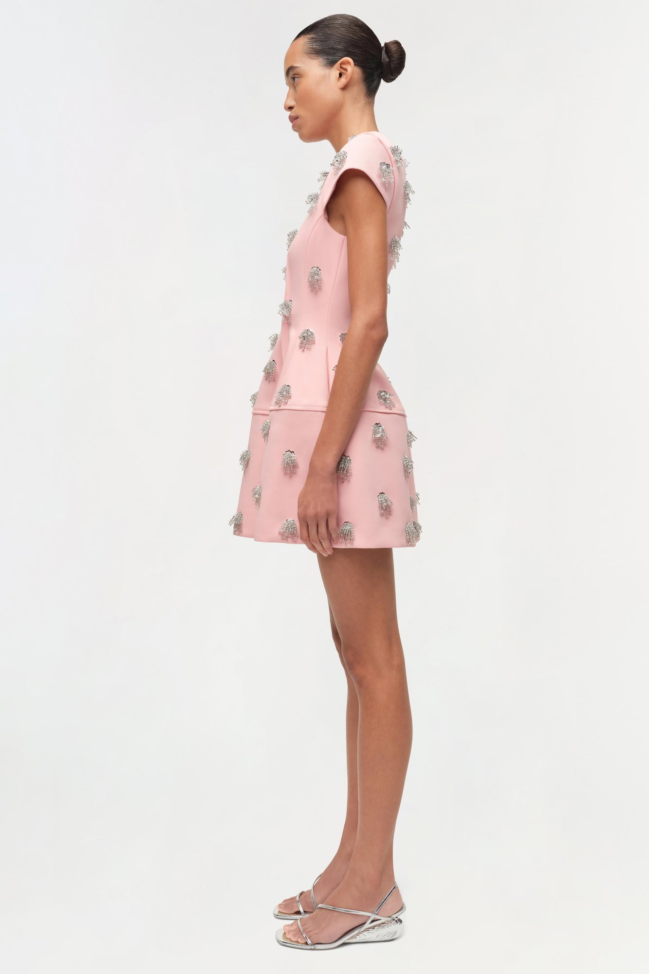 Pink sleeveless mini dress with silver beaded embellishments throughout, shown on model in side profile.