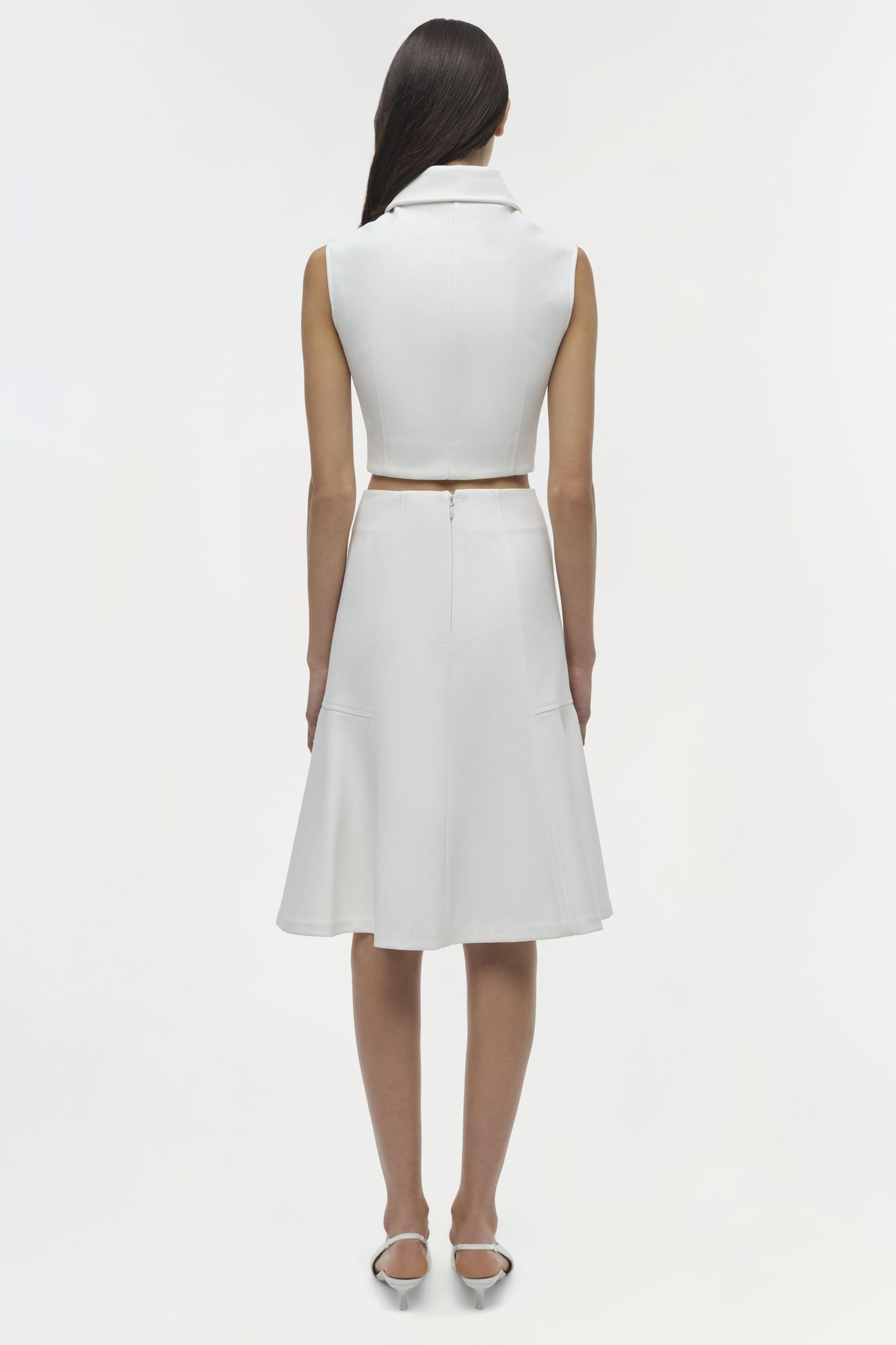 White sleeveless collared top with cutout at waist, worn with matching skirt, shown from back view.