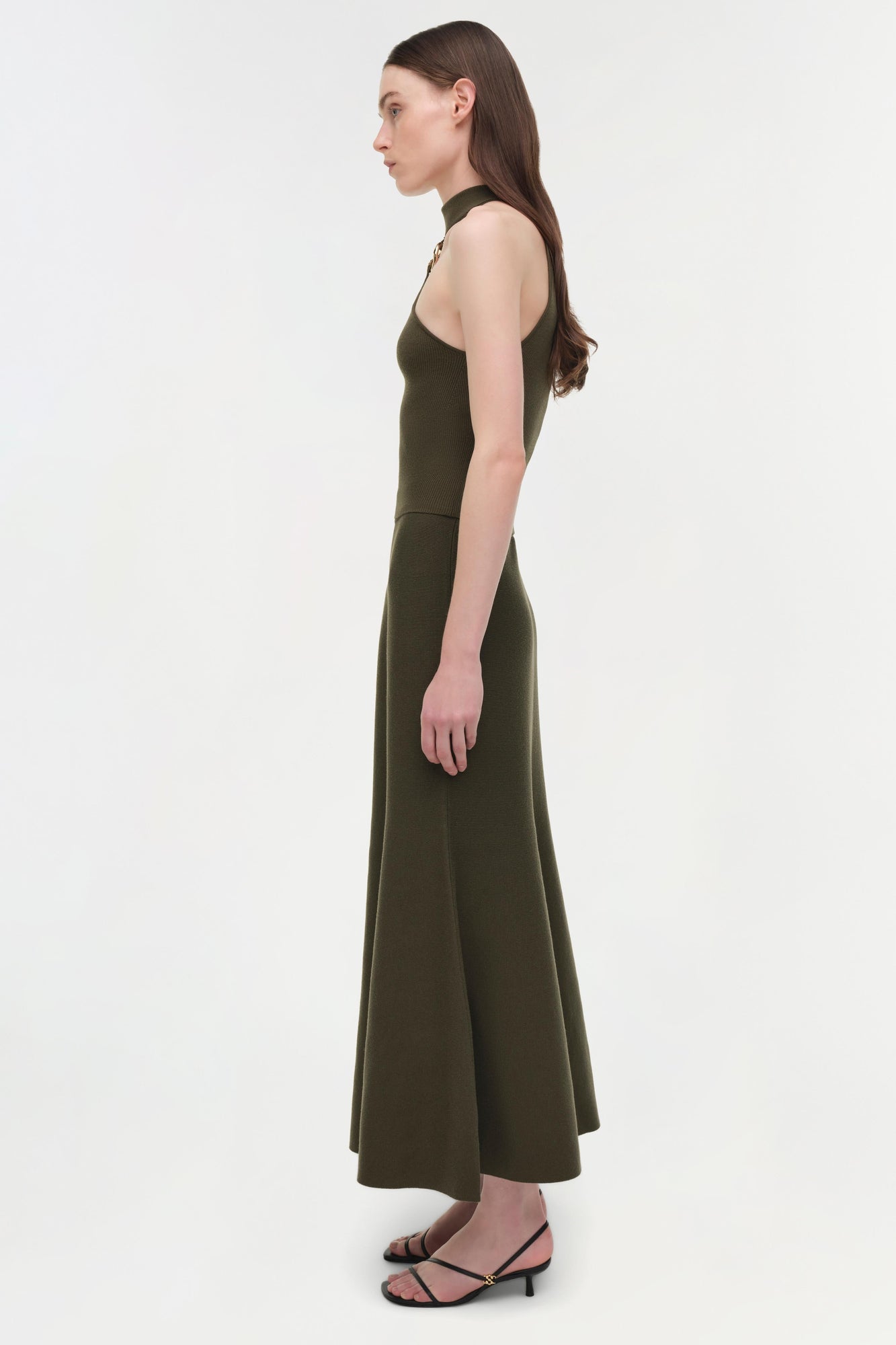Olive green sleeveless halter dress with a fitted bodice and flowing midi skirt, shown on a model in profile view.