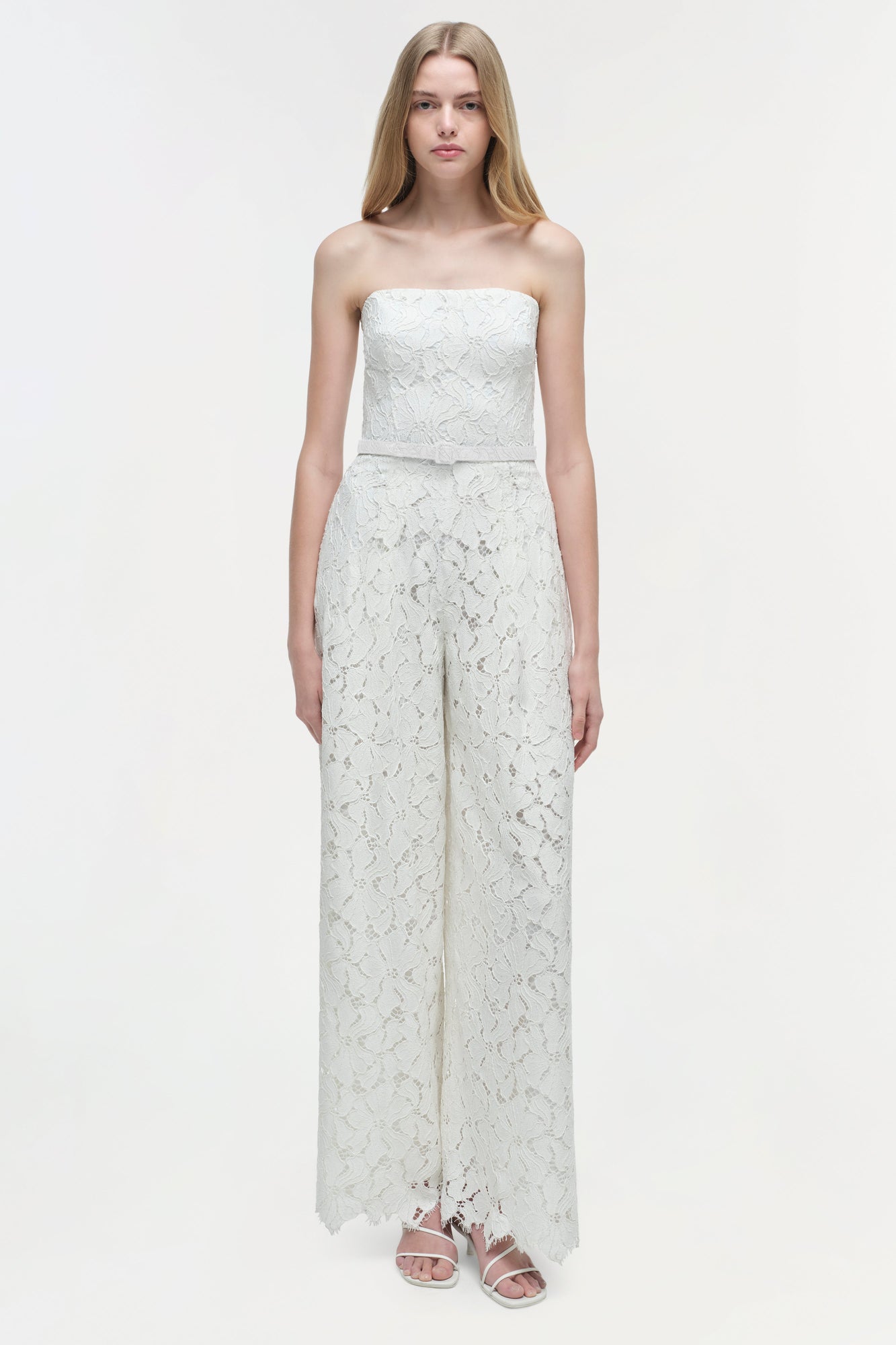 White lace strapless jumpsuit with wide legs and lace trim hem worn with white sandals.