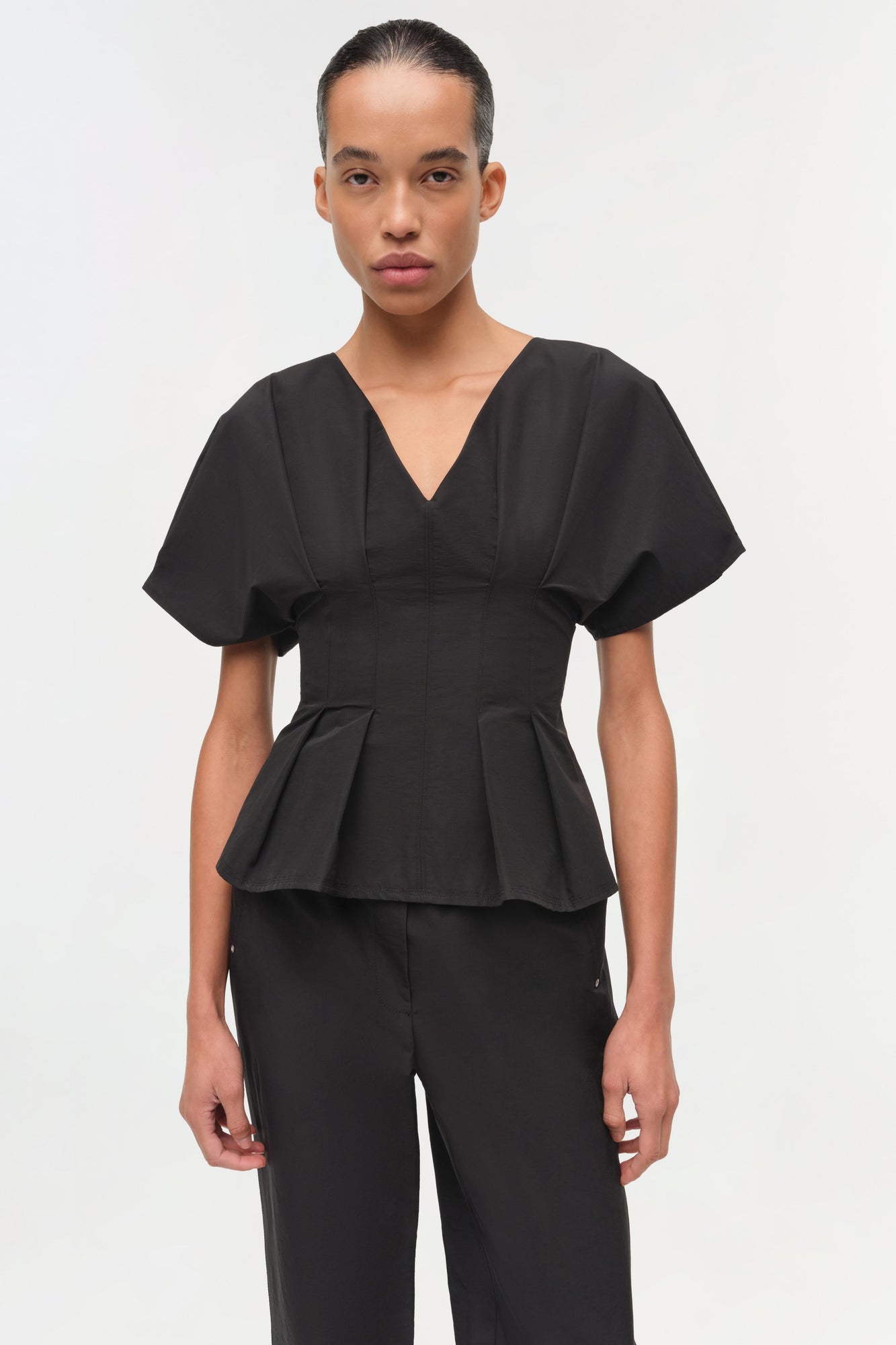 Black cotton faille top with V-neckline, short puffed sleeves, and structured peplum waist detail.