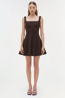 Black sleeveless mini dress with square neckline and fitted bodice, worn with black strappy sandals.