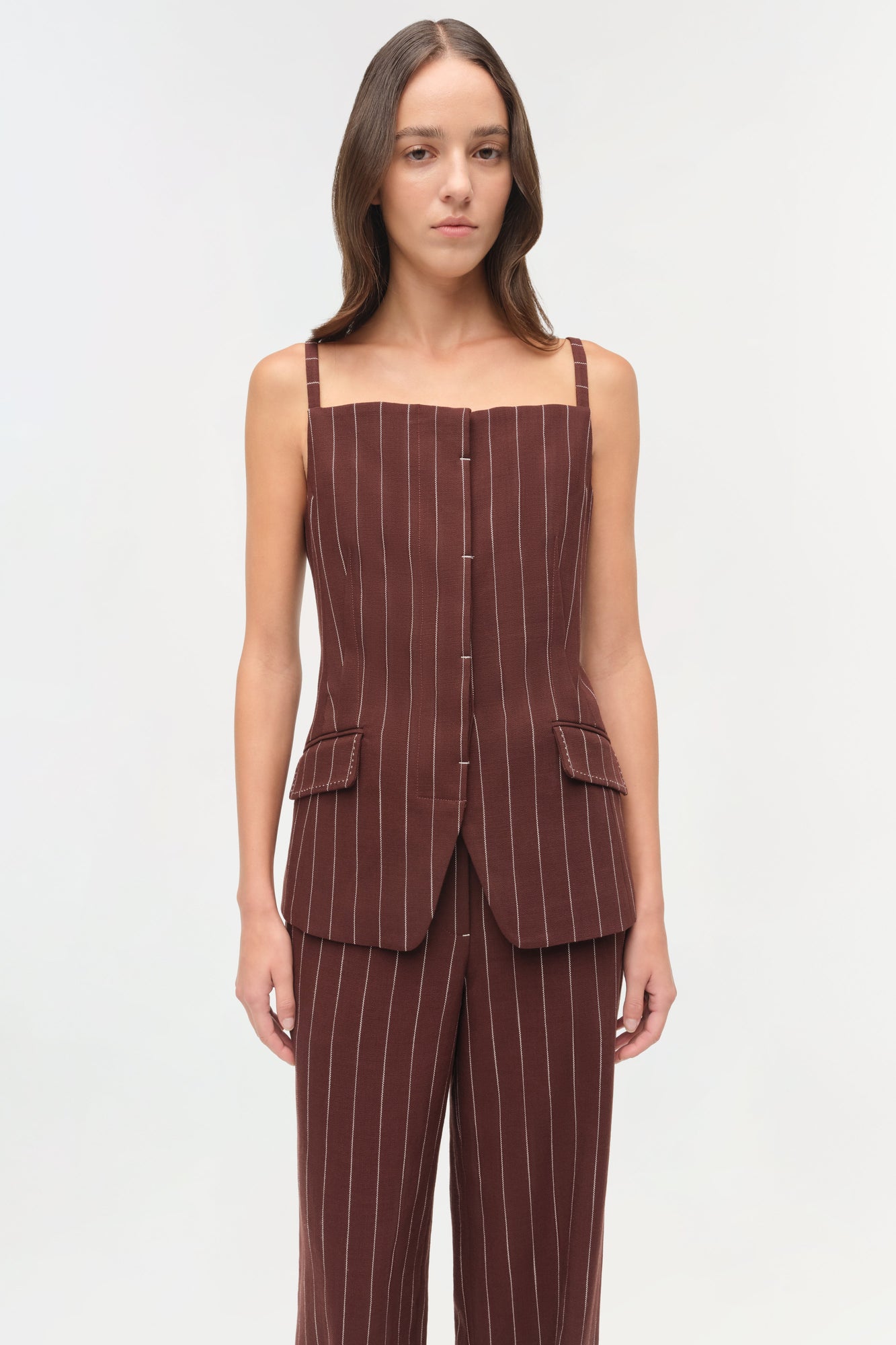 Woman wearing burgundy pinstriped suiting pants with matching sleeveless vest featuring front pockets.