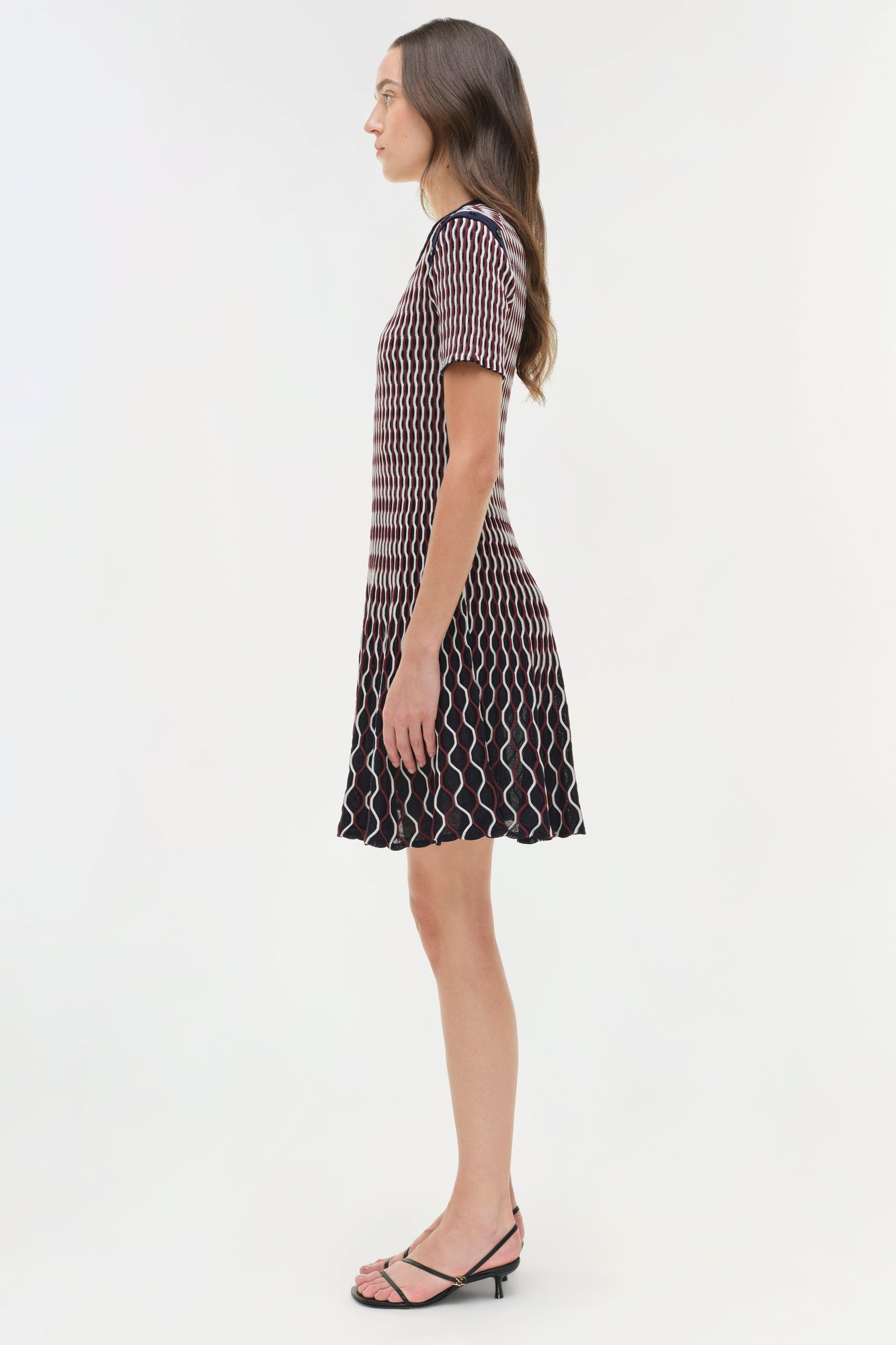 Woman wearing a dark navy knit mini dress with white wavy stripe pattern and short sleeves, shown in side profile view.