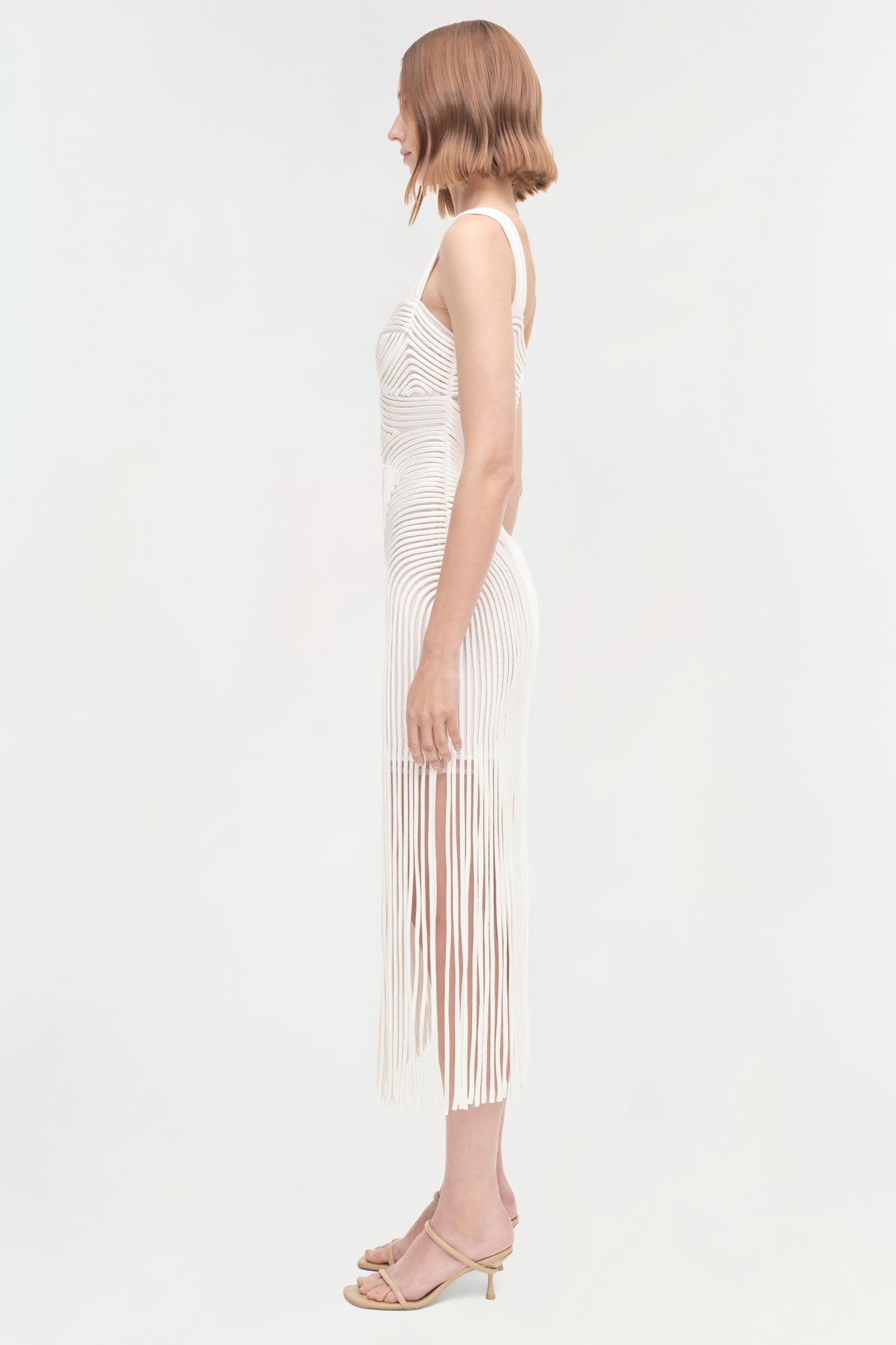 White sleeveless dress with pleated skirt and wavy texture pattern, shown on model from side view.