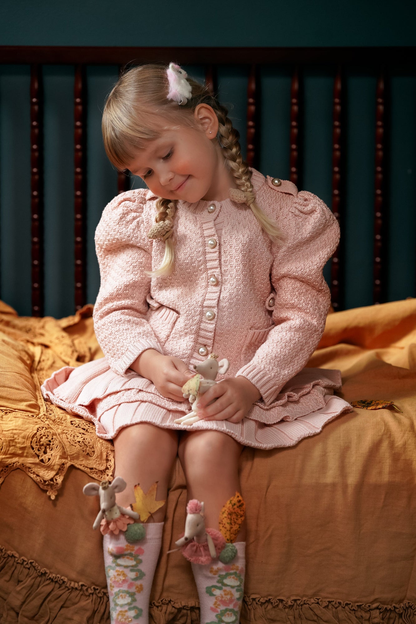 Girl wearing Julie pink knit cotton top and ruffle skirt set while seated, showcasing puff sleeves and feminine knit details