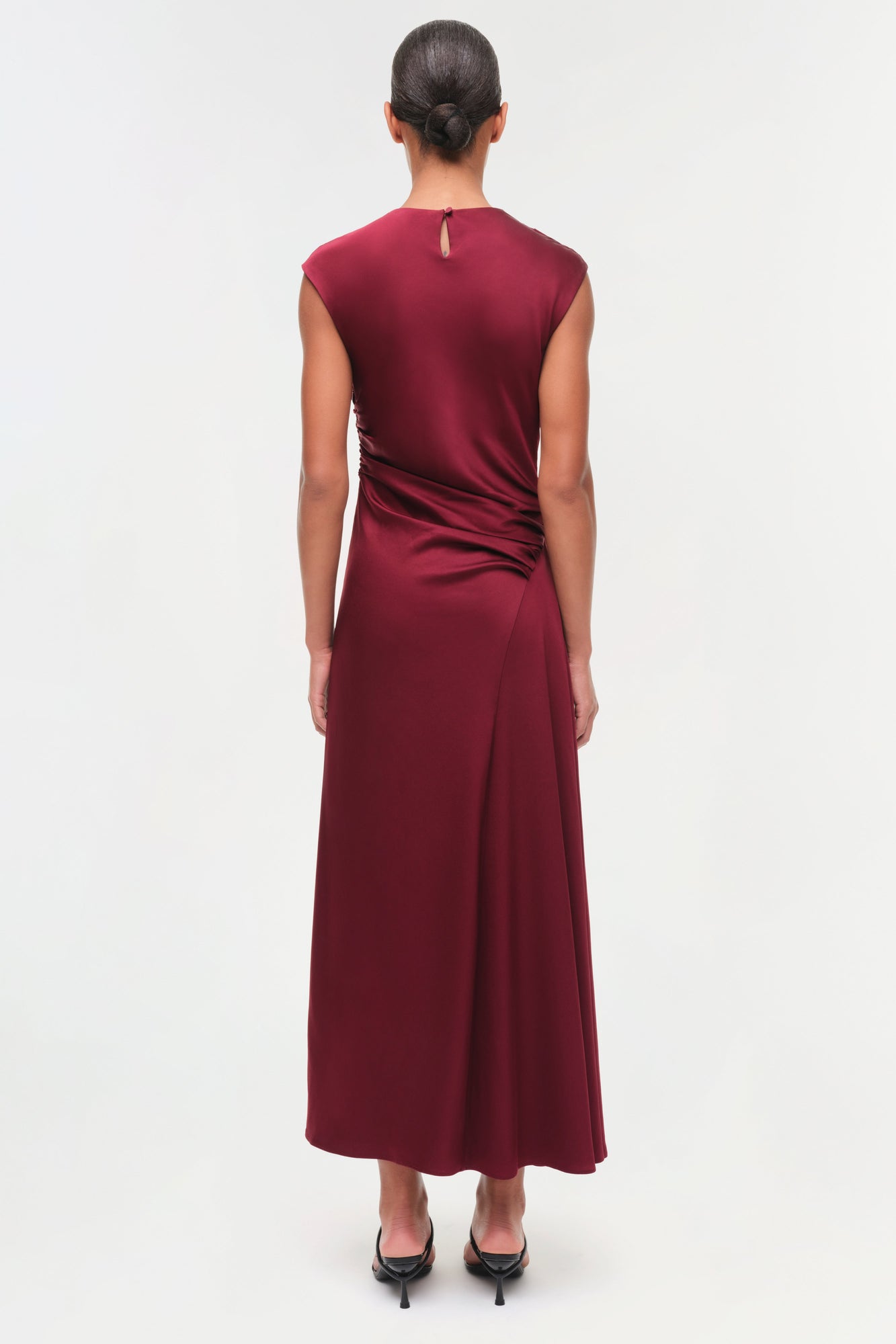 Burgundy satin midi dress with draped side ruching, sleeveless cut, and keyhole back detail on model.