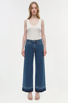 Woman wearing white sleeveless tank top and blue wide-leg cropped jeans with darker hem.
