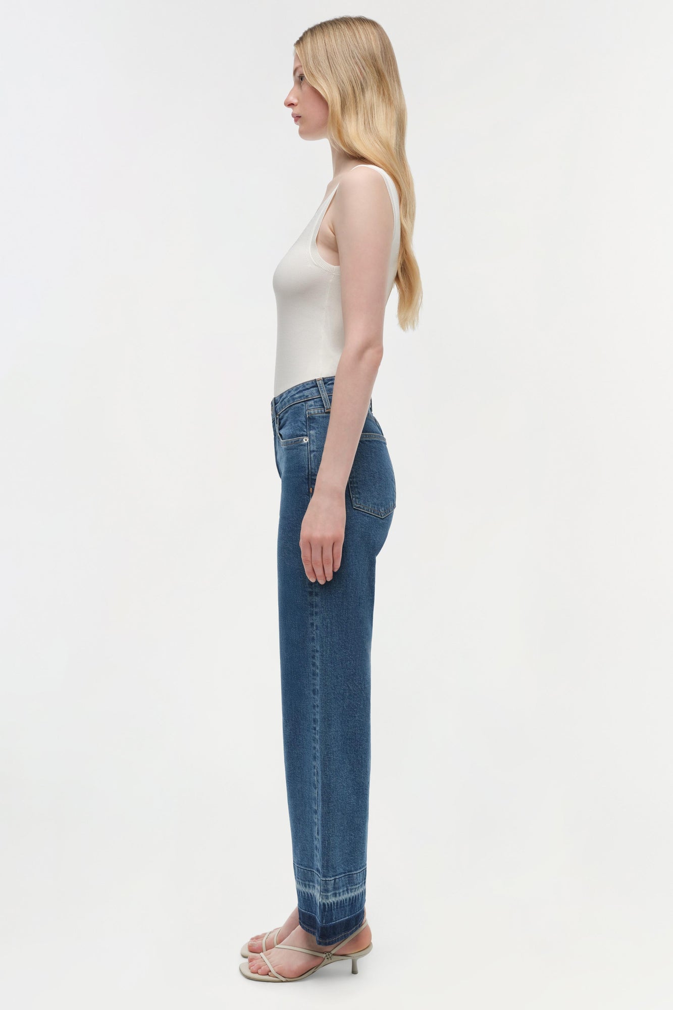 Woman wearing a white sleeveless tank top and blue wide-leg cropped jeans with a raw hem.