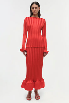 Woman wearing red ribbed long-sleeve top with ruched cuffs and matching midi skirt with ruffled hem.