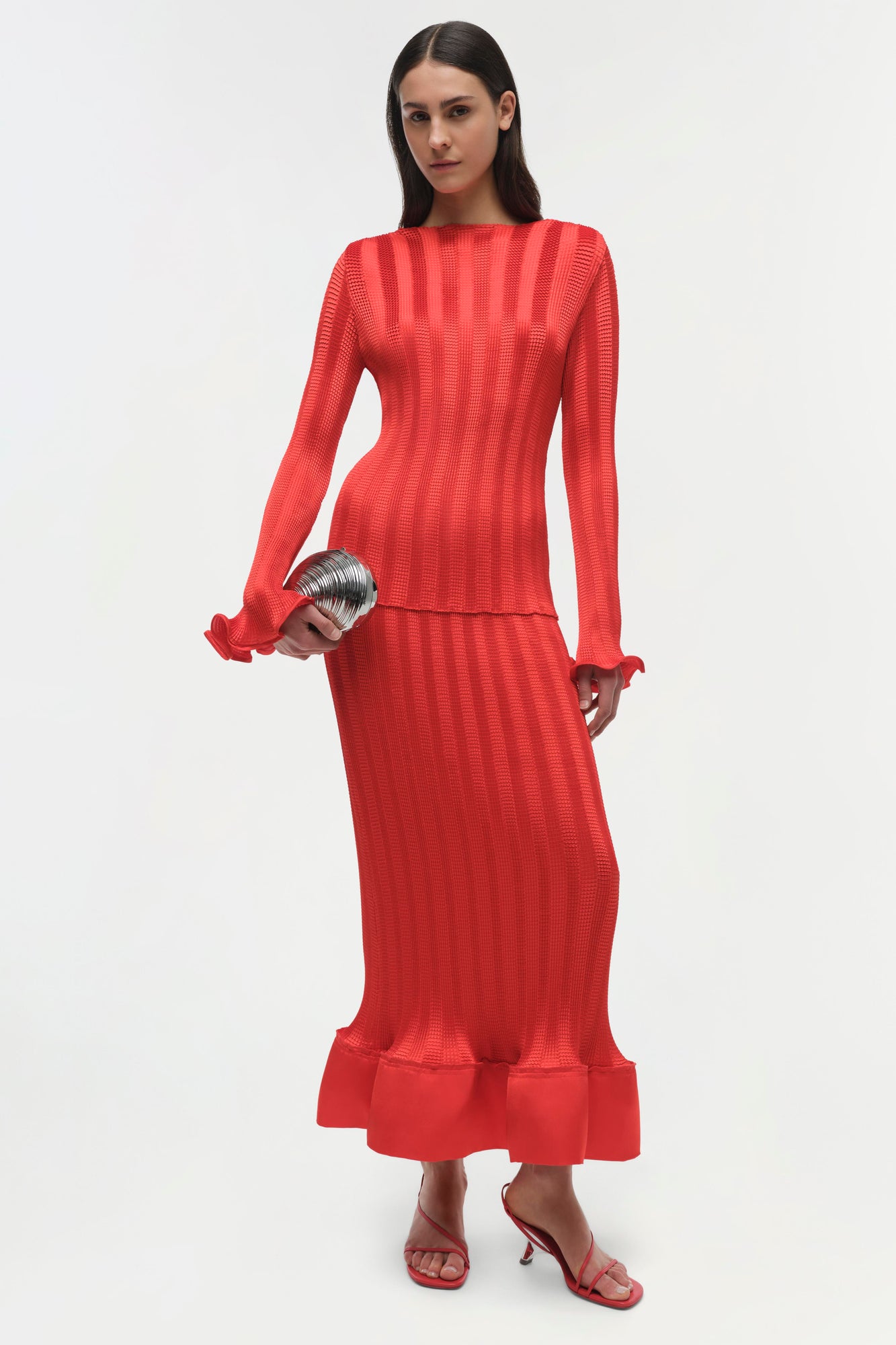 Woman wearing a red ribbed long-sleeve top with ruffled cuffs and matching maxi skirt with ruffle hem.