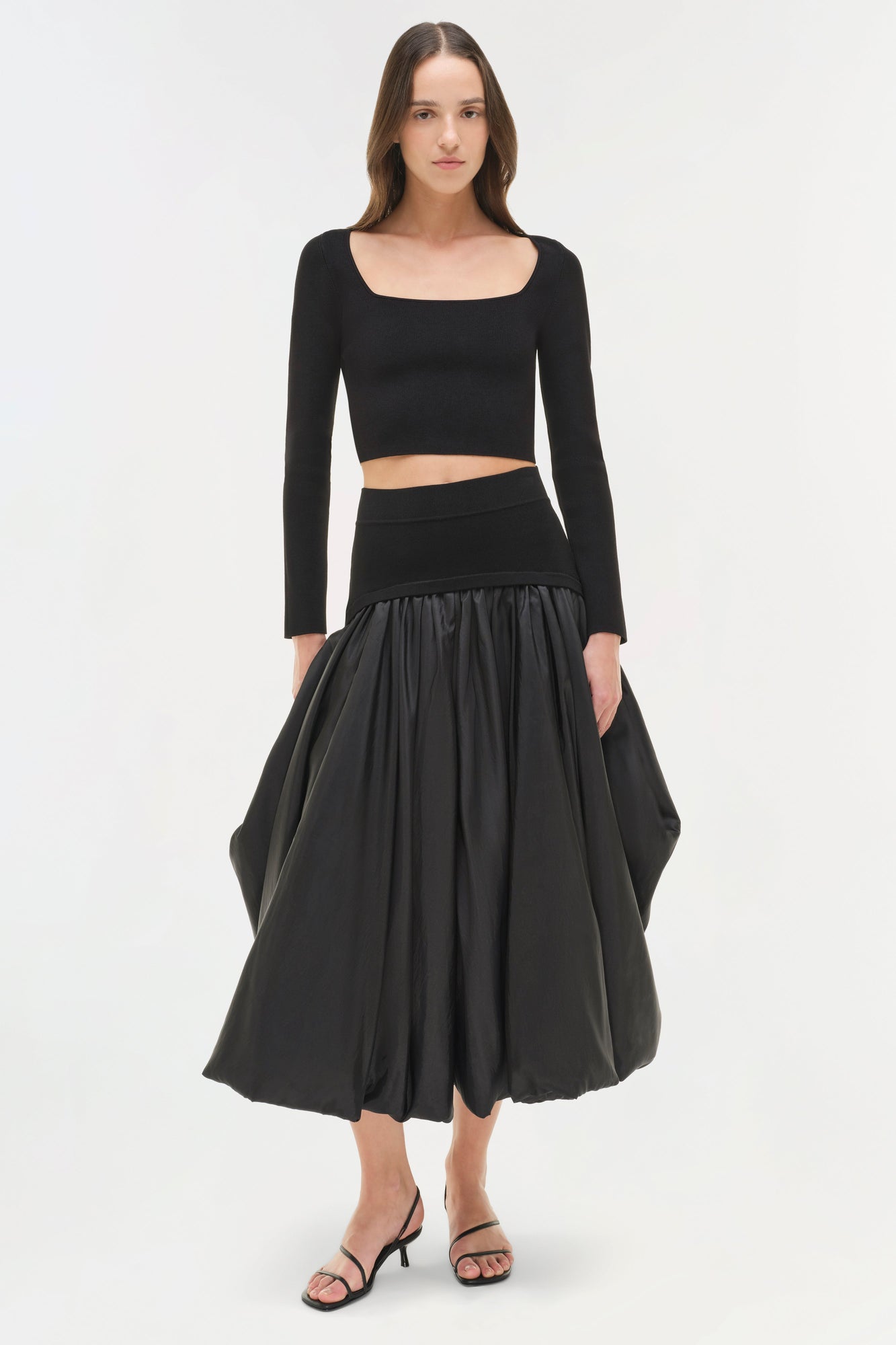 Black knit cropped top with long sleeves and square neckline worn with matching waistband and full skirt.