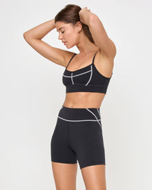Side view of the LSPACE Star Power Shorts in black on a model against a white background, paired with the matching black Eclipse Bra, showing the profile of the high-waist bike shorts.