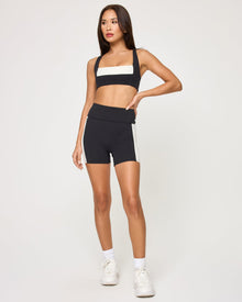 Front view of the LSPACE Uppercut Bra in black-cream on a model against a white background, showing the square-neck sports bra with cream trim, paired with matching black-cream high-rise active shorts.