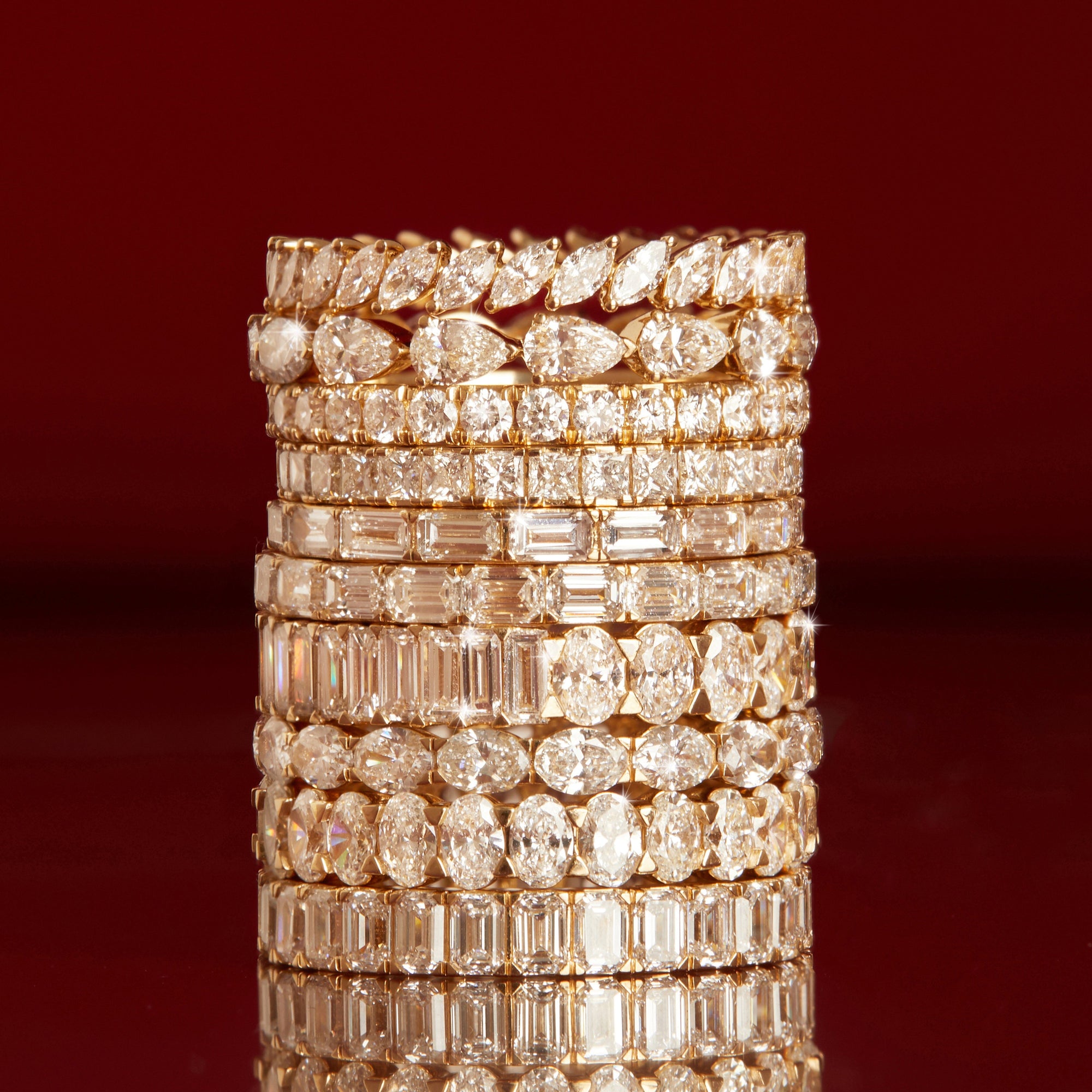Flatlay Model A tall stack of mixed-cut gold and diamond eternity rings on a dark red background