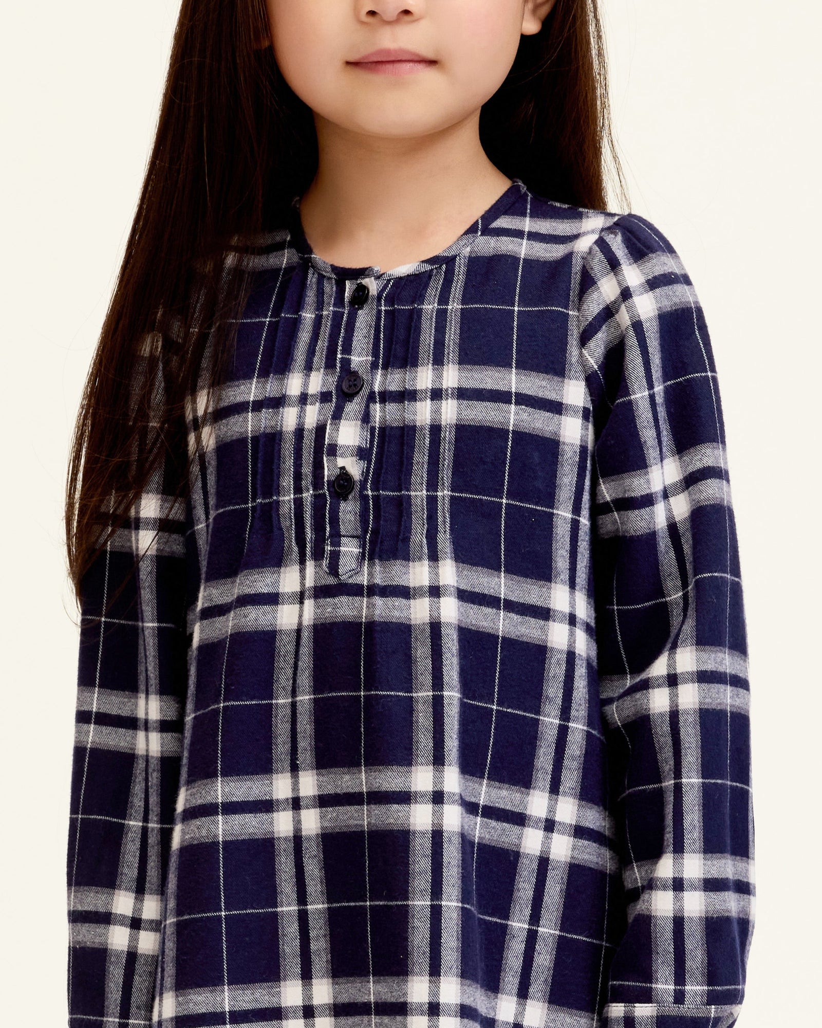 The Girl's Brushed Twill Beatrice Nightgown in Oxford Tartan features a navy, white, and gray plaid pattern, long sleeves, a round neckline, front buttons, and pleats near the chest.
