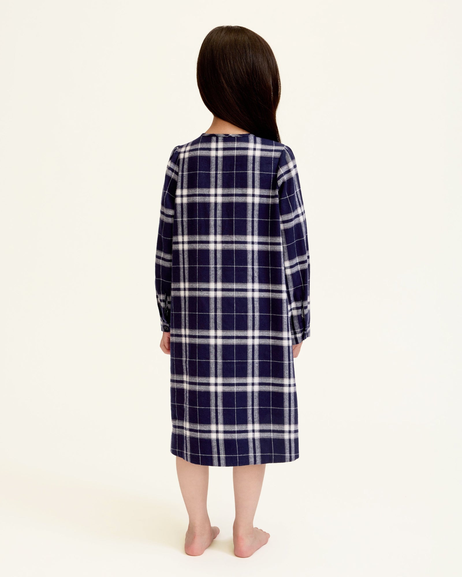 The Girl's Brushed Twill Beatrice Nightgown in Oxford Tartan features a navy, white, and gray plaid pattern, long sleeves, a round neckline, front buttons, and pleats near the chest.