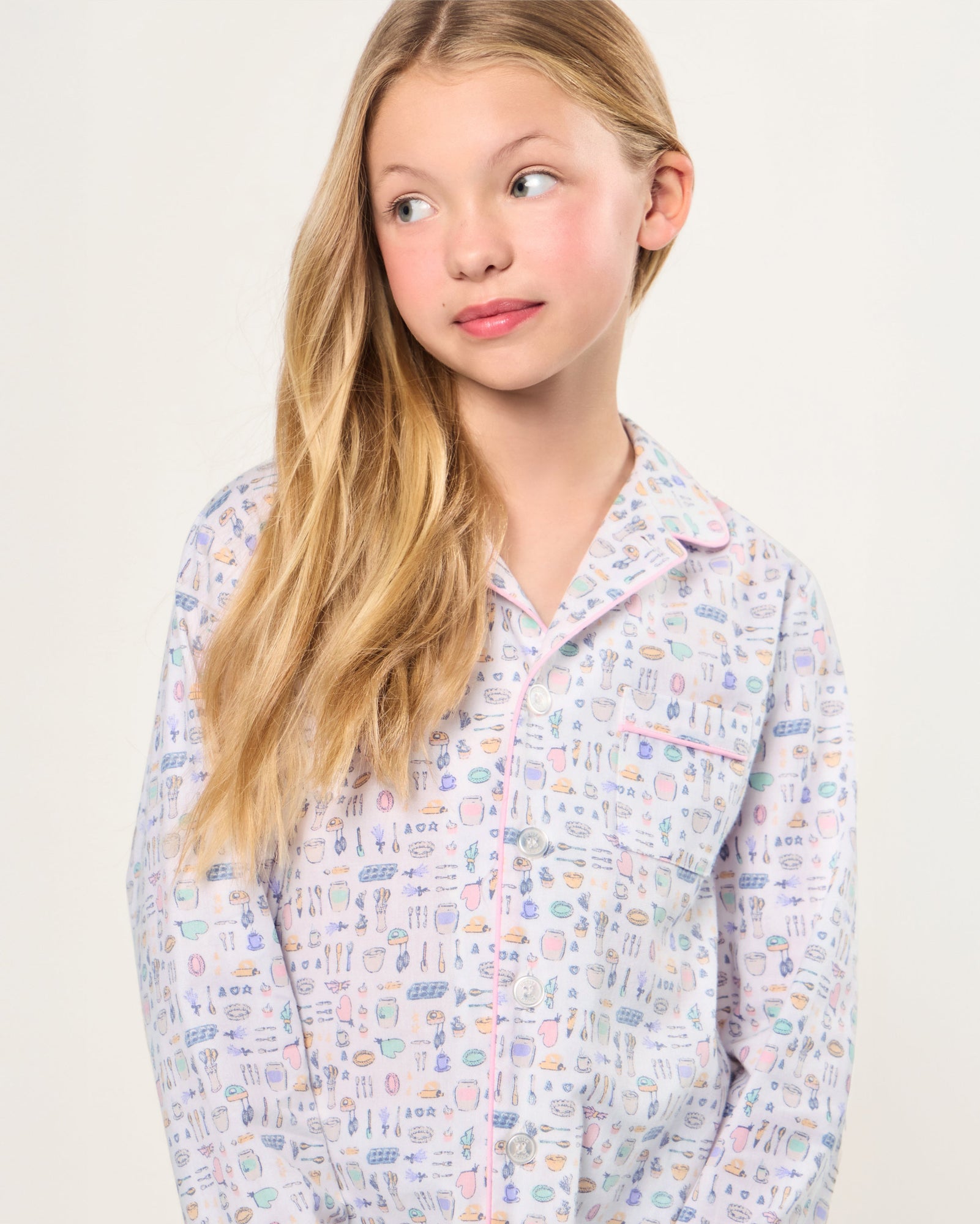The Kid's Twill Pajama Set in Baking Spirits Bright features white long-sleeve button-up top and long pants with a colorful print of various small household and travel items.